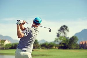 Golfer hitting golf shot with club on course while on summer vac
